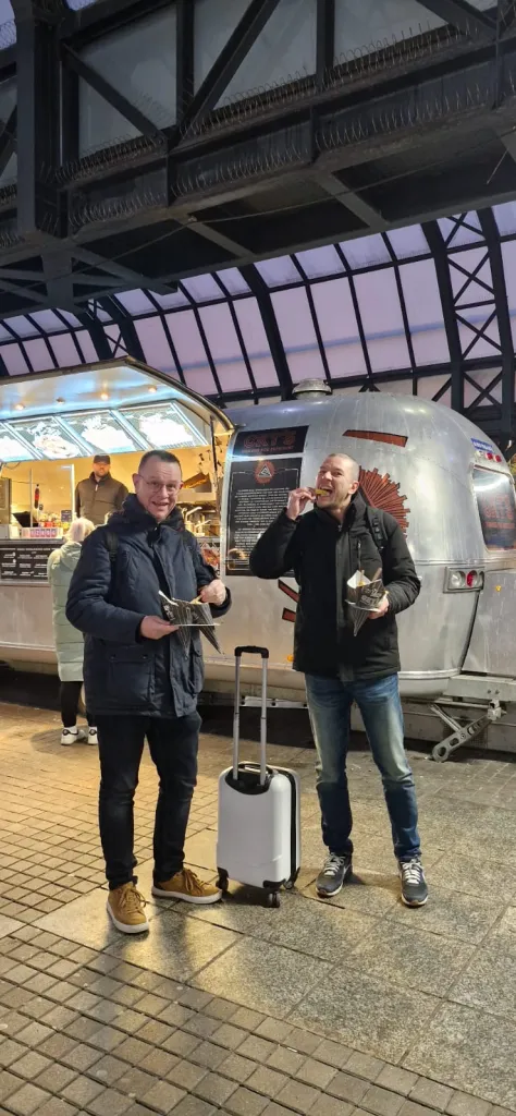 Two travellers eating street food with a suitcase at a station
